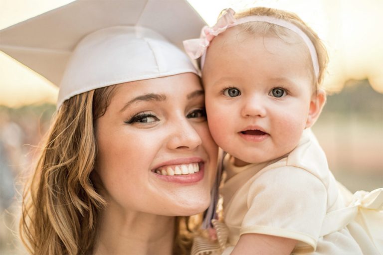 young white mother in graduation cap holding baby girl and smiling